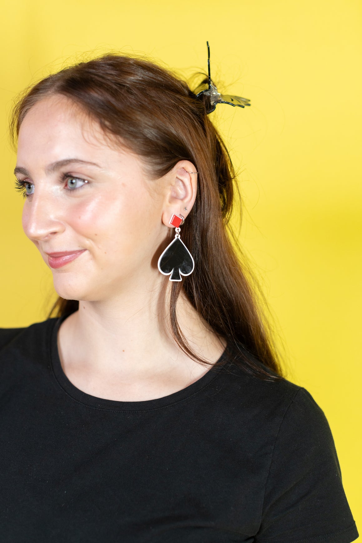 Person with long hair wearing black and red hair clips against a yellow background