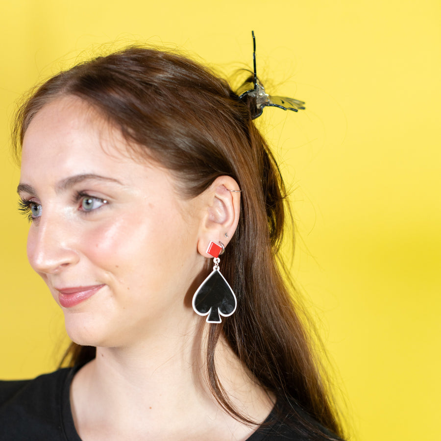 Pair of earrings with club and spade symbols on a 'cheerful' branded card against a red background