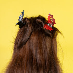 Person with long hair wearing black and red hair clips against a yellow background