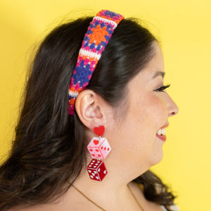 Woman wearing colorful headband and red dice-shaped earrings against a yellow background