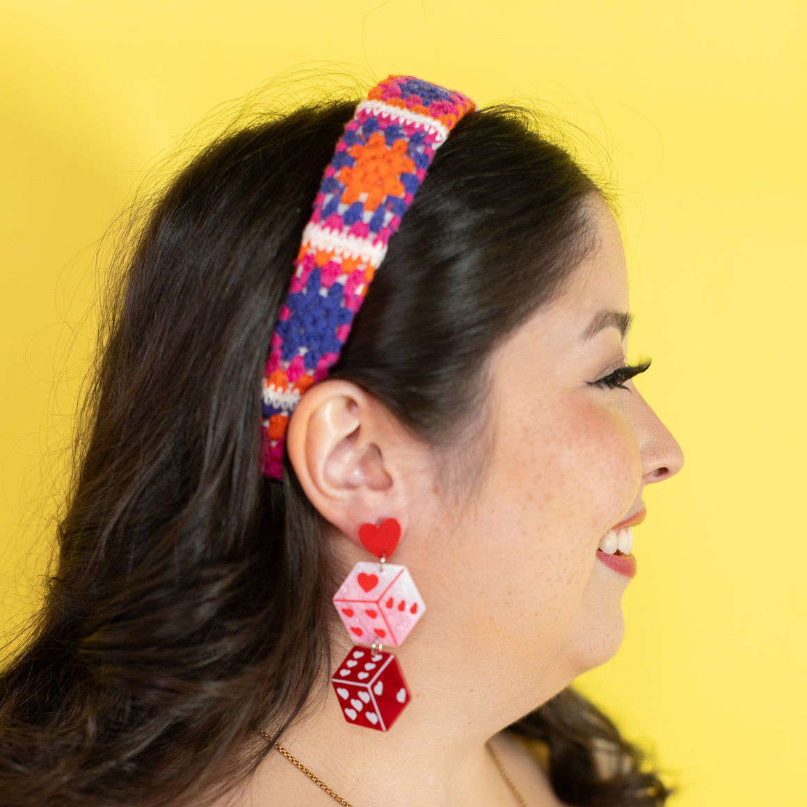 Woman wearing colorful headband and red dice-shaped earrings against a yellow background