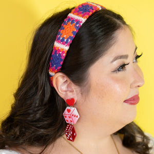 Woman wearing a colorful headband and red earrings against a yellow background