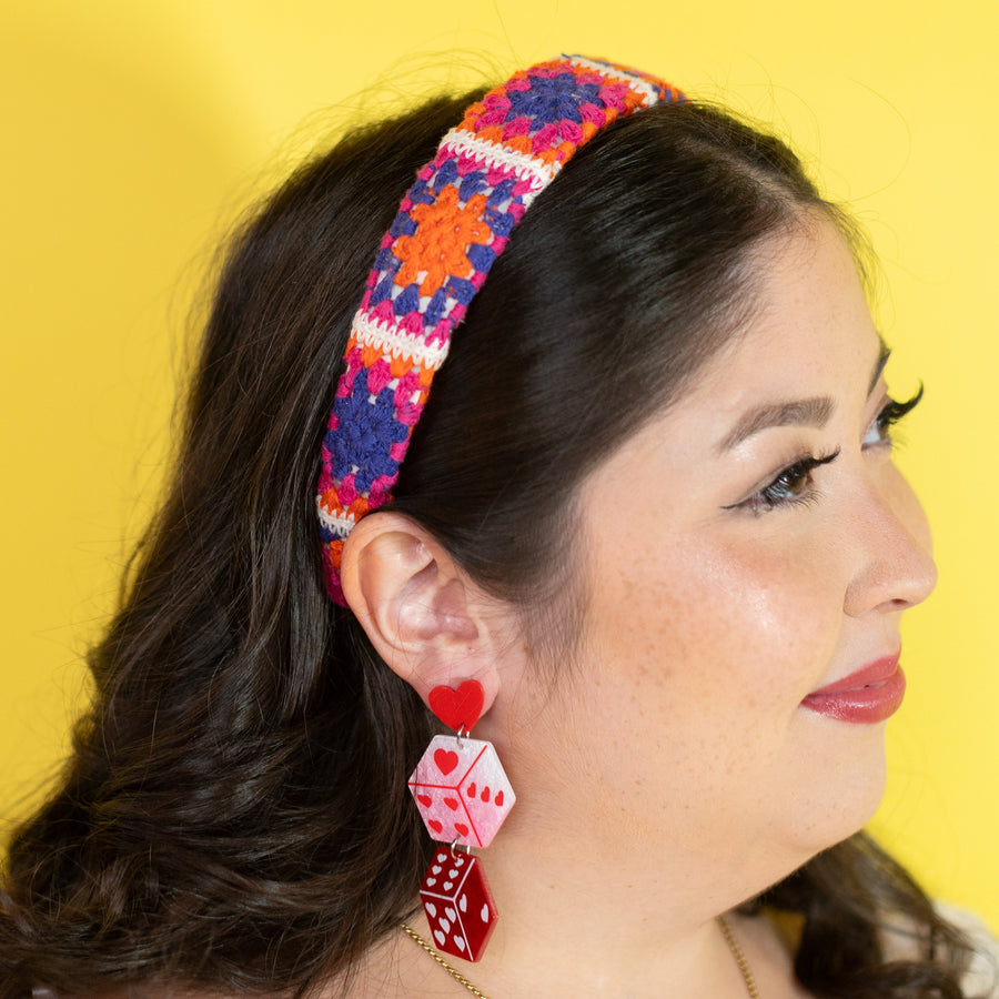 Woman wearing colorful headband and red dice-shaped earrings against a yellow background