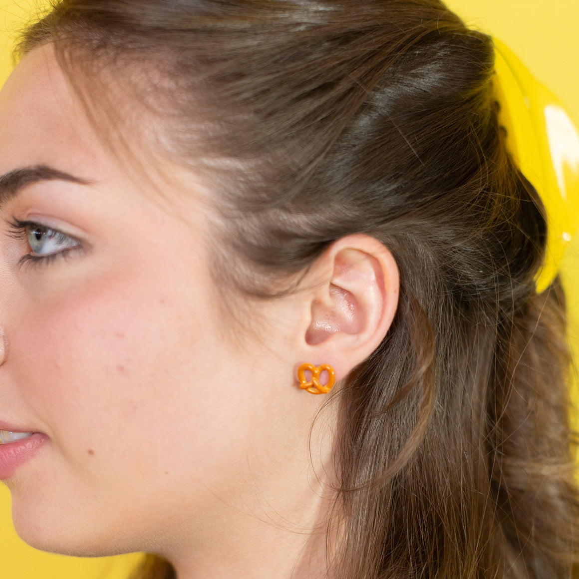 Close-up of a person wearing orange heart-shaped earrings against a yellow background
