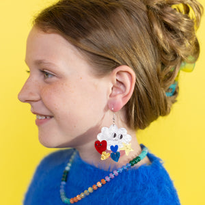 Girl wearing colorful earrings and a blue sweater against a yellow background