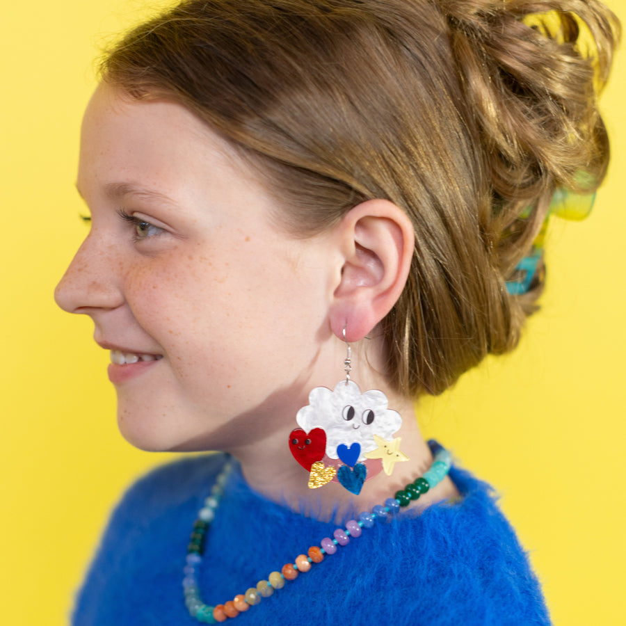 Pair of cloud-shaped earrings with colorful accessories on a 'cheerful' branded card against a pink background.