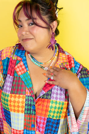 Person wearing a colorful patterned outfit with jewelry against a yellow background