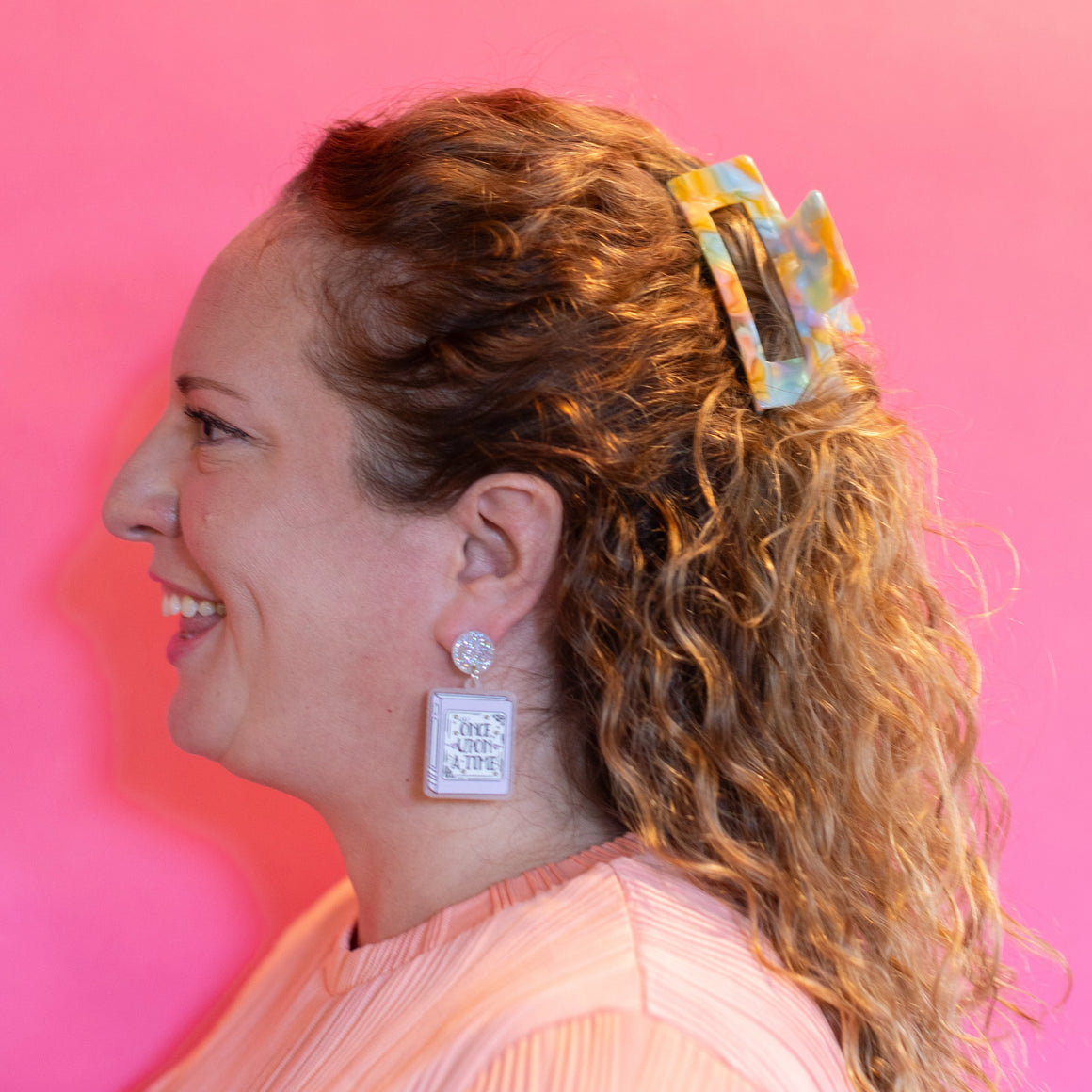 Woman with curly hair wearing a colorful scrunchie, smiling against a pink background