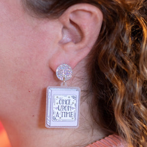 Close-up of a woman wearing earrings with text on them, against a blurred background.