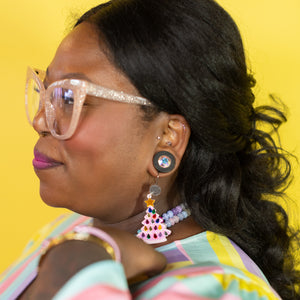 Woman wearing colorful glasses and earrings against a yellow background