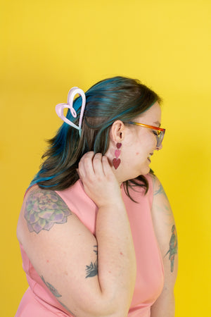 Person with blue hair and tattoos wearing a pink sleeveless top against a yellow background