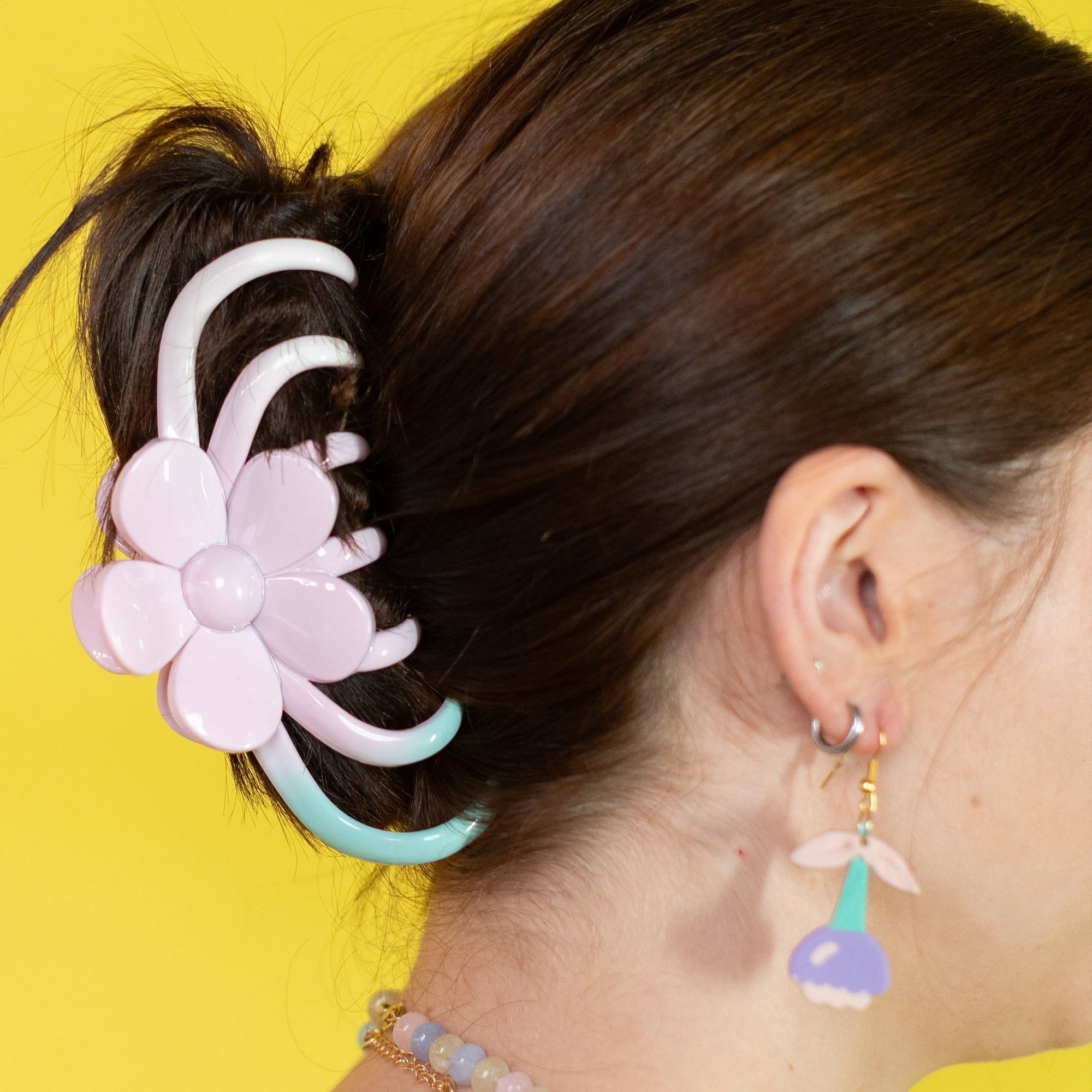 Person with a floral hair accessory and colorful earrings against a yellow background