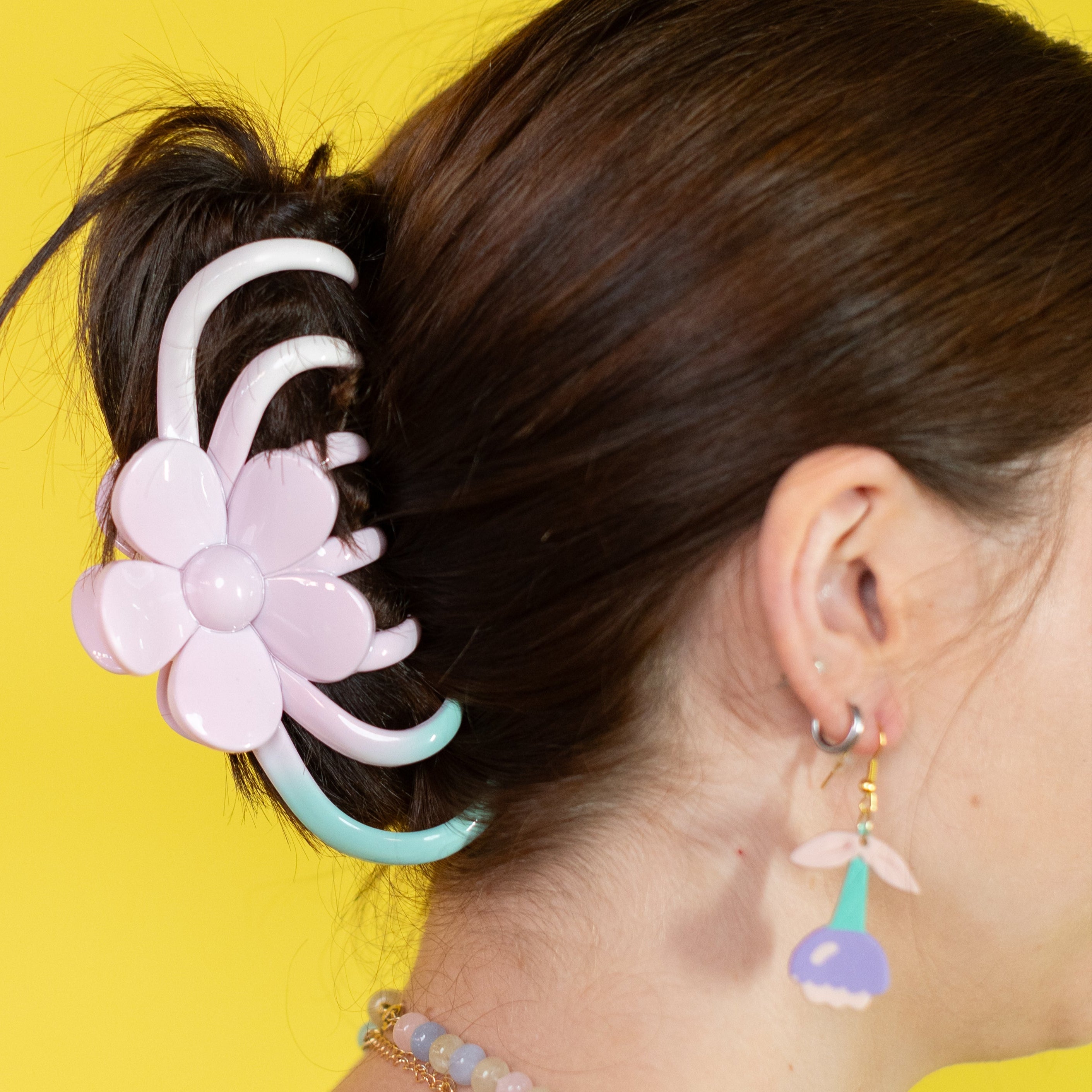 Person with a floral hair accessory and colorful earrings against a yellow background