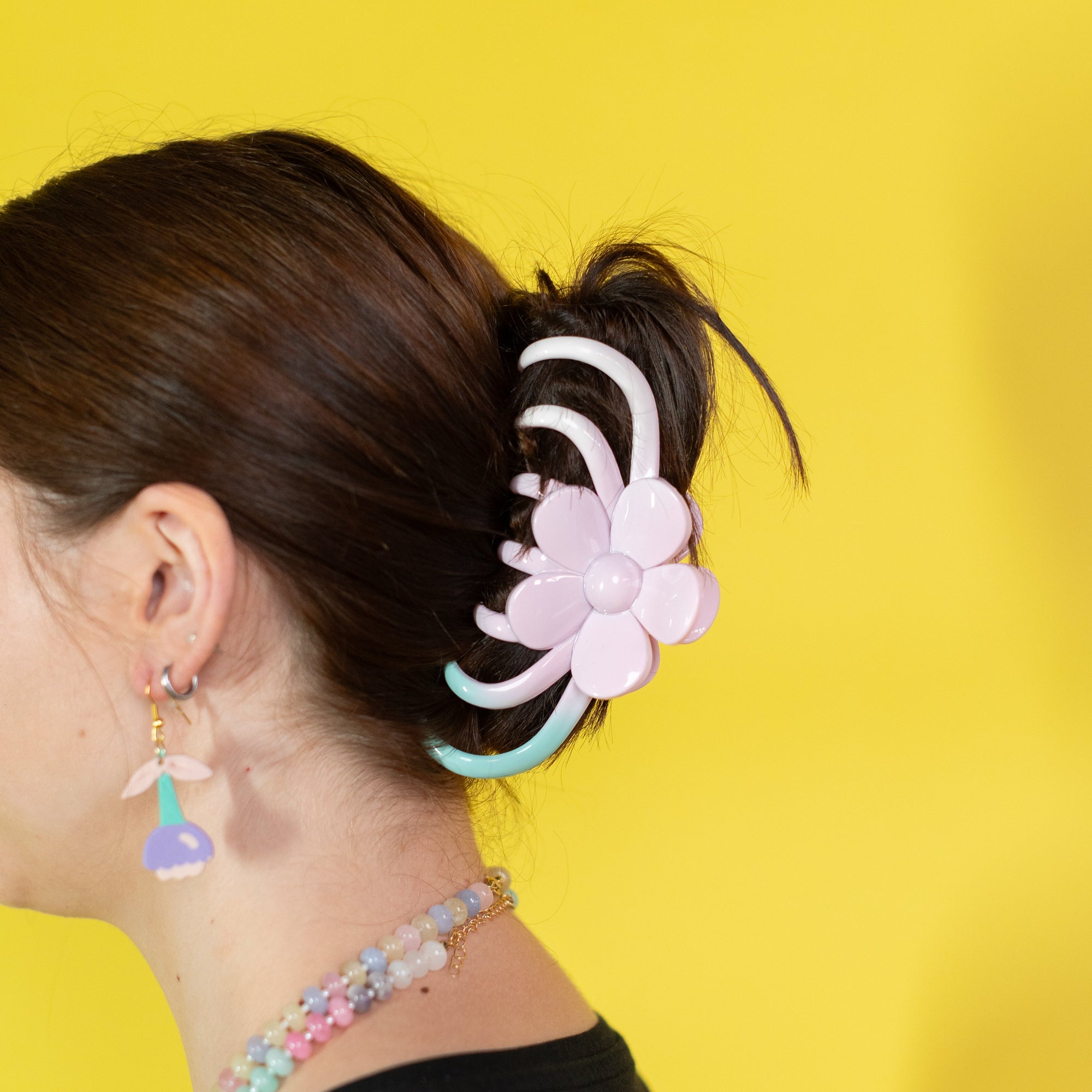 Person with a floral hair accessory and colorful earrings against a yellow background