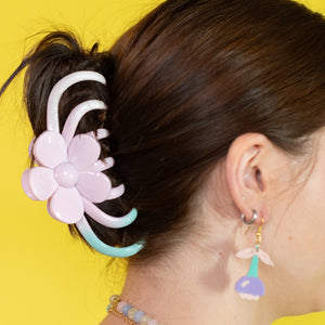 Person with a floral hair accessory and colorful earrings against a yellow background