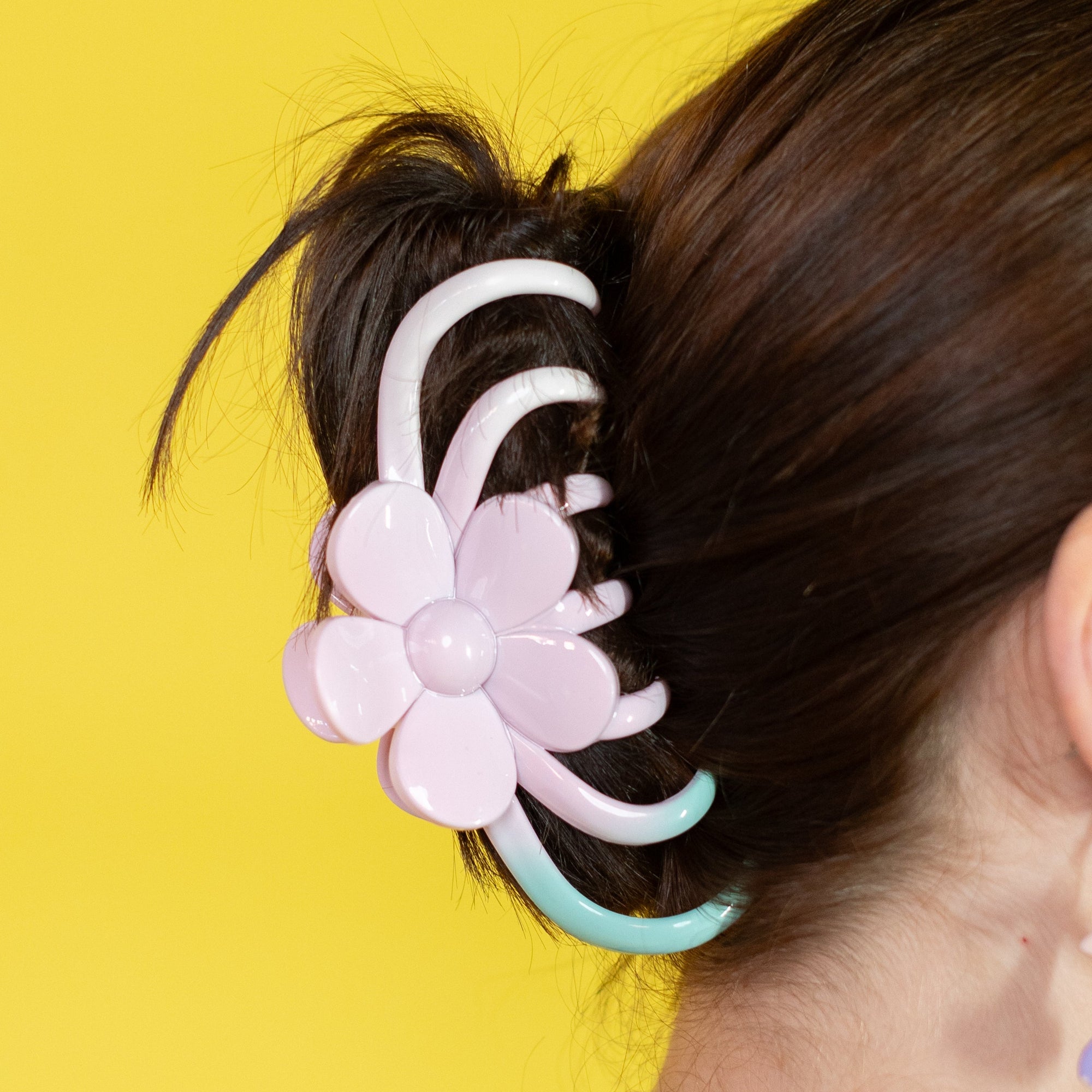 Person with a floral hair accessory and colorful earrings against a yellow background