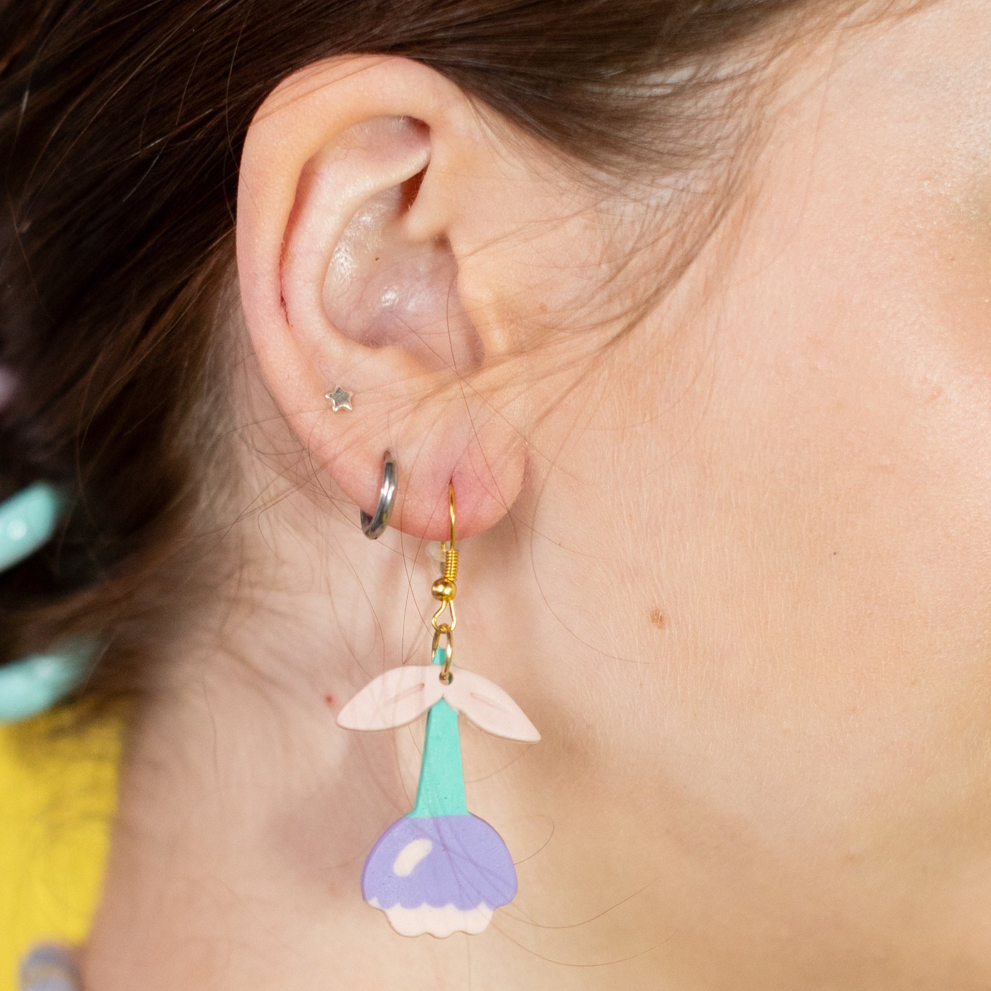 Woman wearing colorful earrings and a necklace against a yellow background