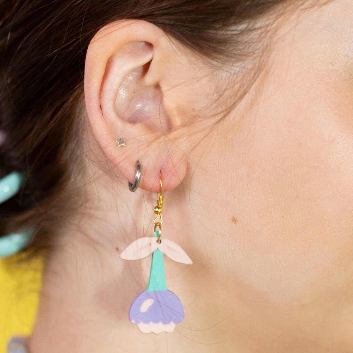Woman wearing colorful earrings and a necklace against a yellow background