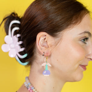 Woman wearing colorful earrings and a necklace against a yellow background