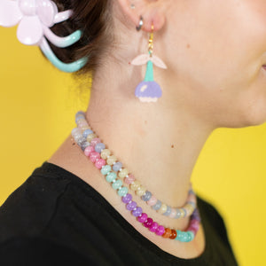 Person wearing colorful beaded necklace and earrings against a yellow background
