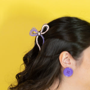 Person with a purple hair clip and earring against a yellow background
