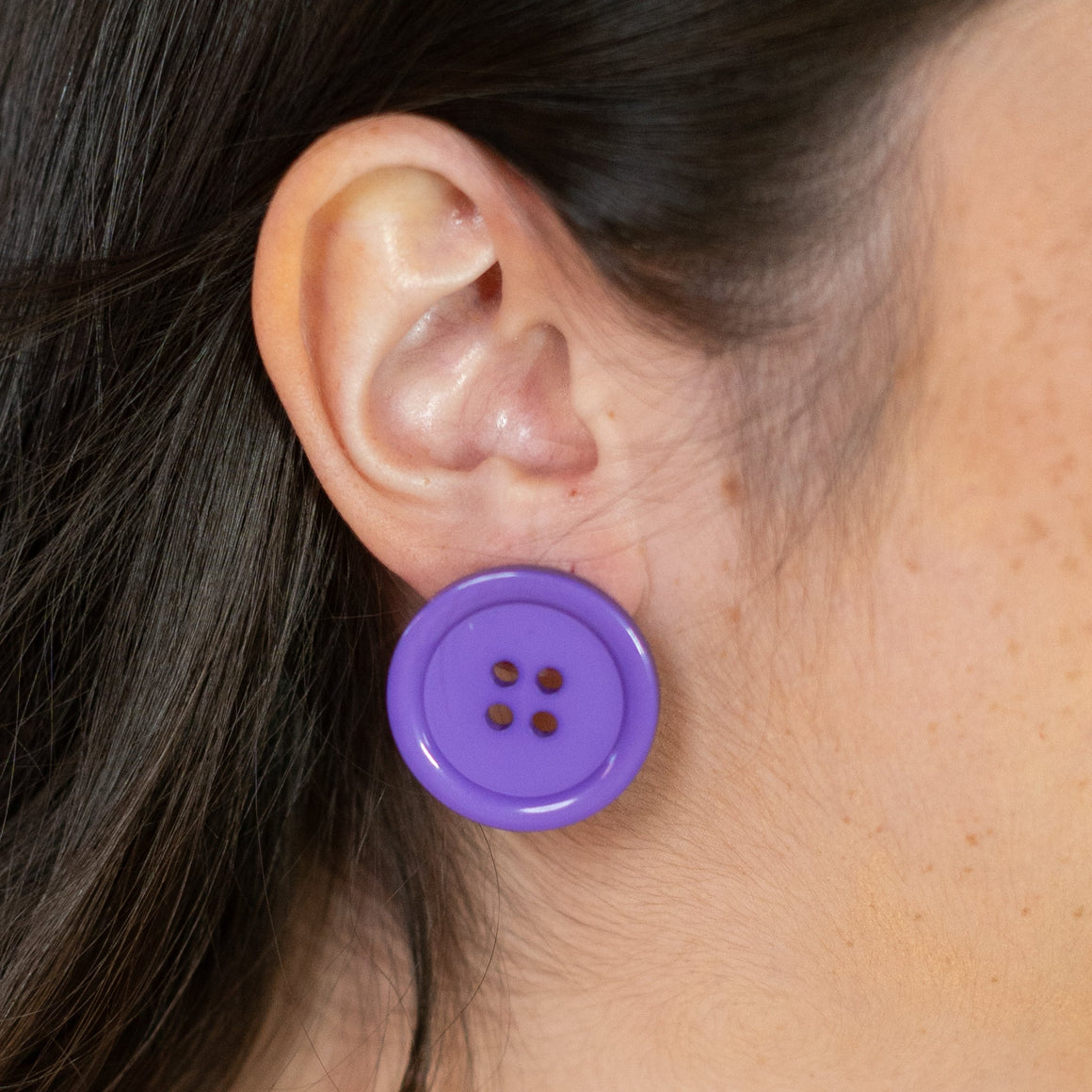 Woman wearing a purple button earring against a yellow background