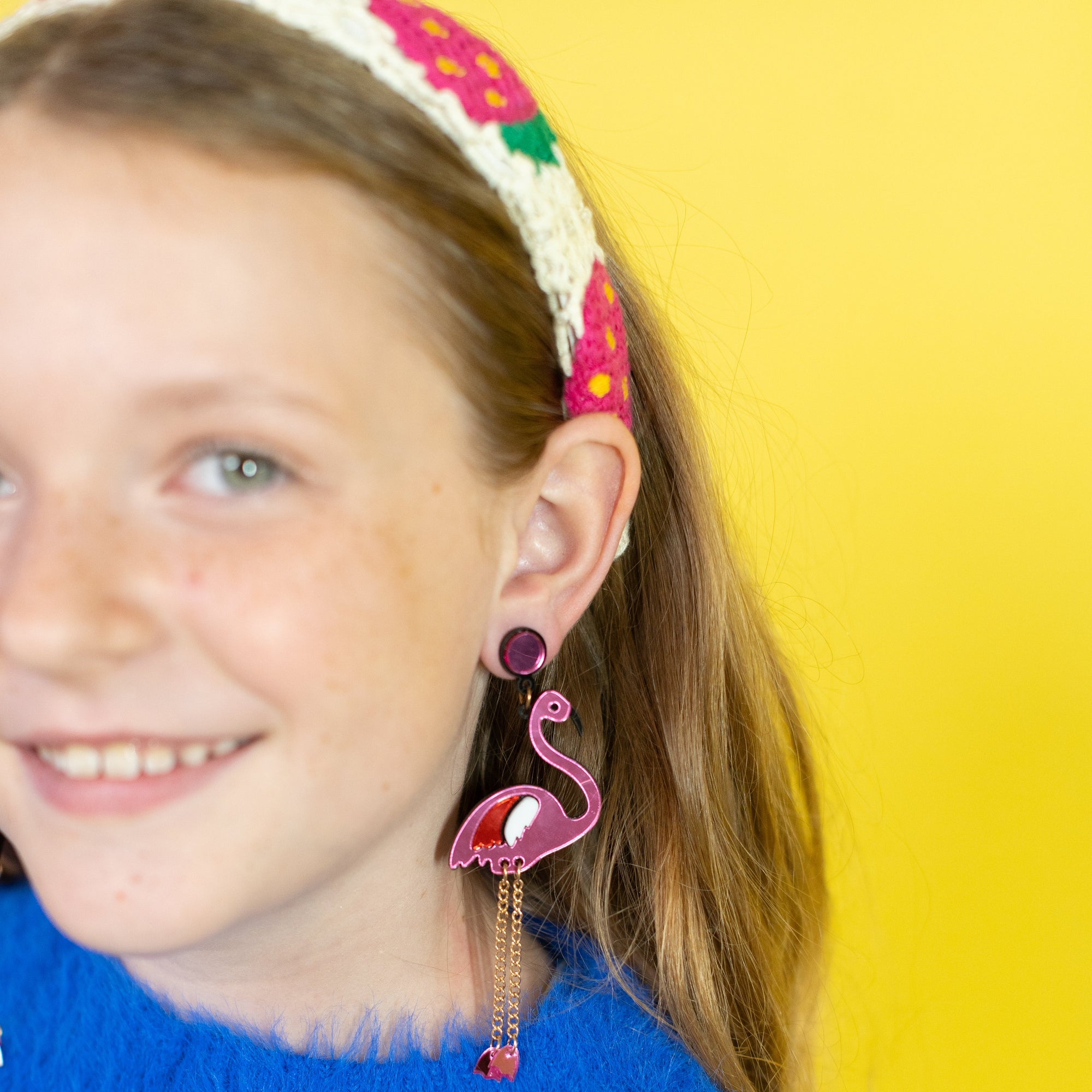 Girl wearing pink flamingo earrings with a yellow background