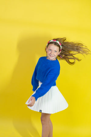 Young girl in a blue sweater and white skirt against a yellow background