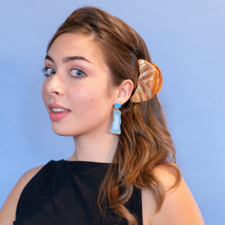 Close-up of a person wearing a marbled hair clip against a blue background