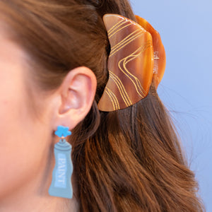 Close-up of a person wearing a marbled hair clip against a blue background