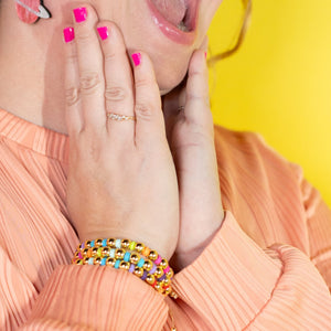 Woman in peach sweater with colorful bracelets on a yellow background