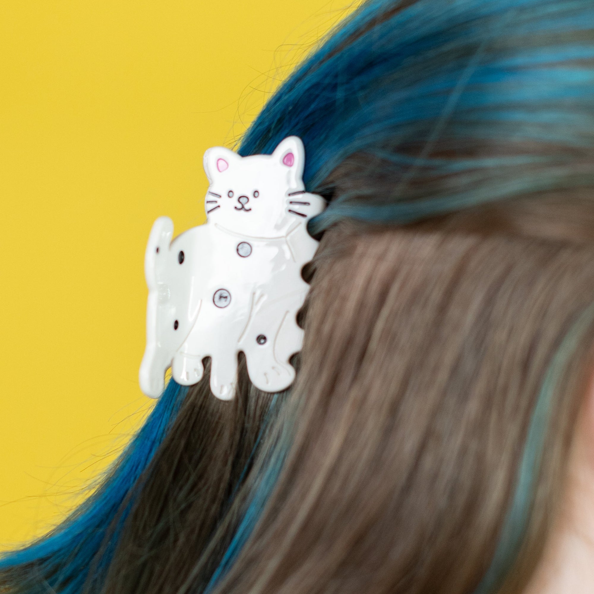 Person with blue hair wearing a white cat-shaped hair clip against a yellow background