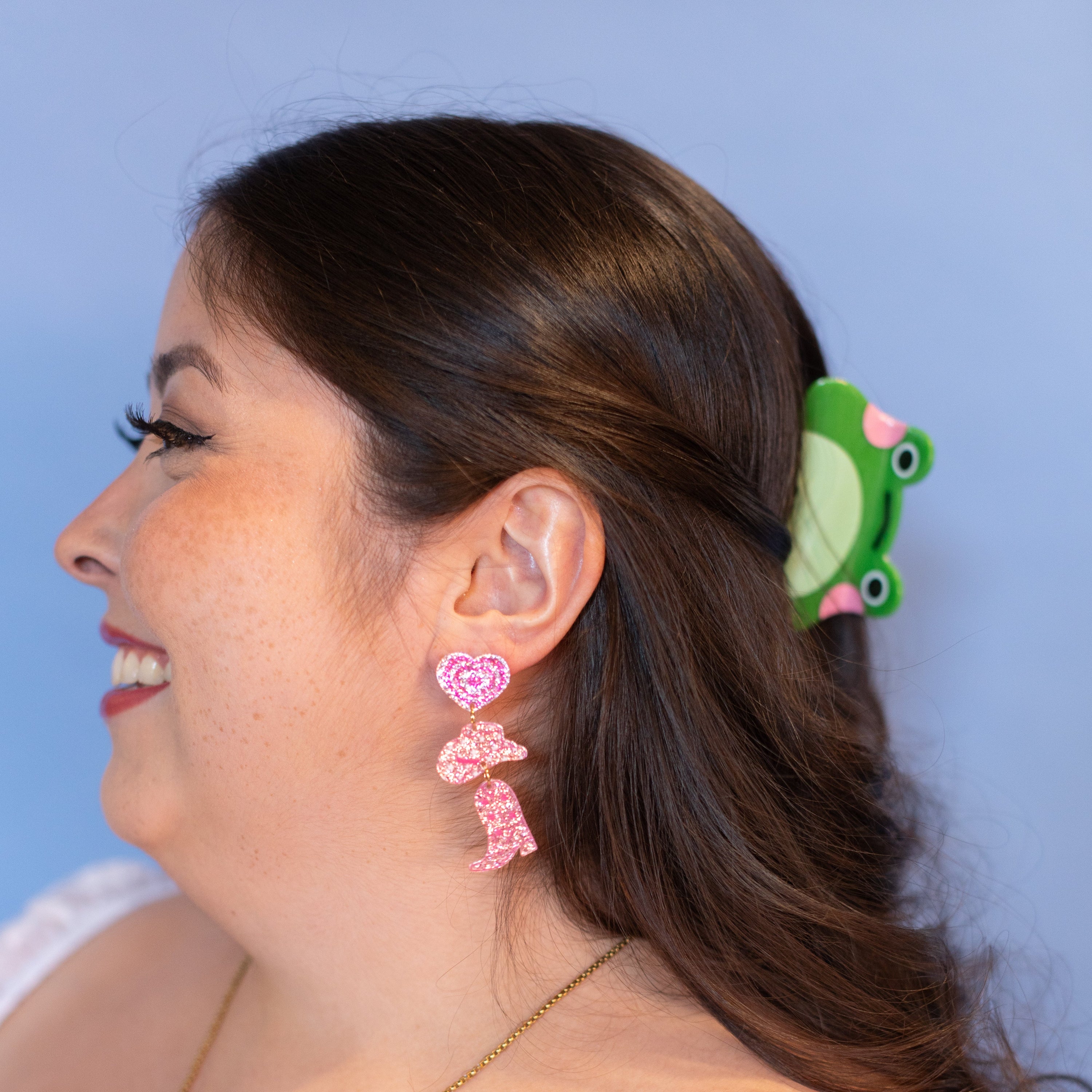 Woman wearing pink earrings and a green hair clip against a blue background
