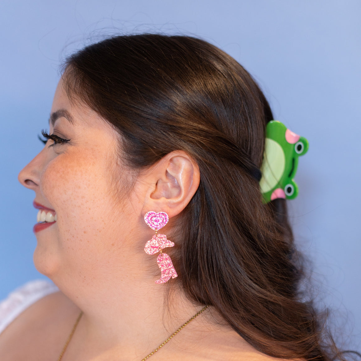 Woman wearing pink earrings and a green hair clip against a blue background
