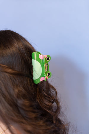 Green frog-shaped hair clip on a person's hair against a light blue background