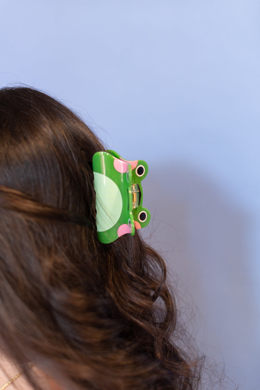 Woman wearing pink earrings and a green hair clip against a blue background