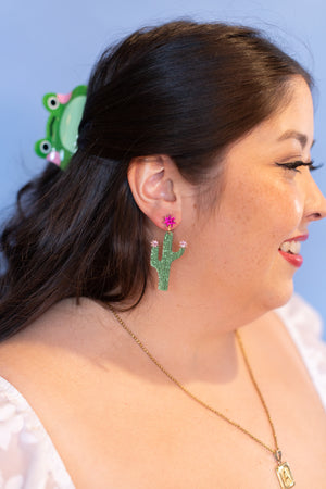 Woman wearing green cactus earrings with a blue background