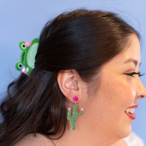 Woman wearing green cactus earrings with a blue background