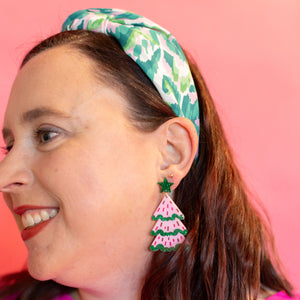 Woman wearing colorful earrings and a headband against a pink background