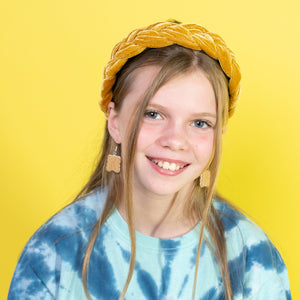 Young girl wearing a blue tie-dye shirt and yellow hat against a yellow background