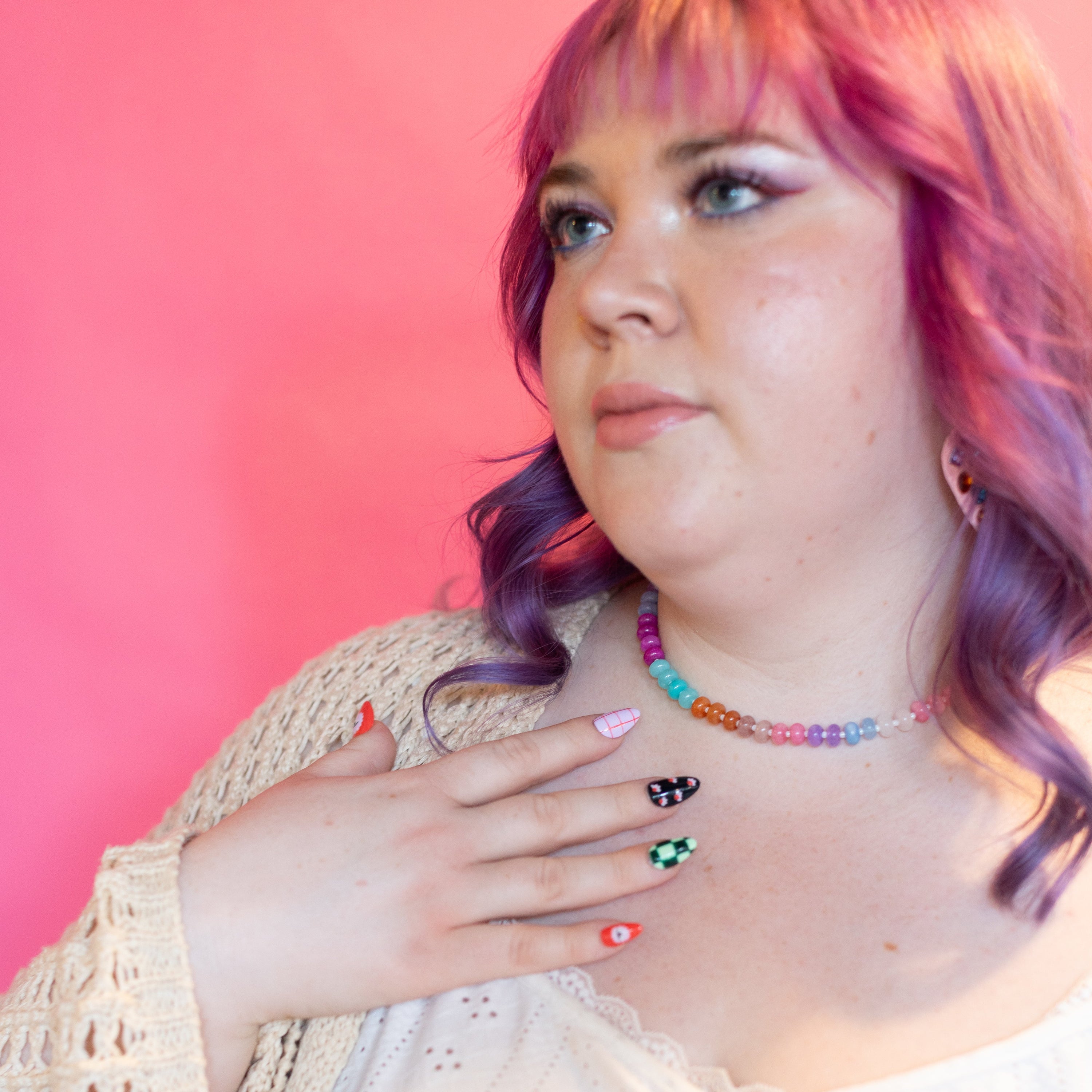 Person with colorful hair and nail polish against a pink background
