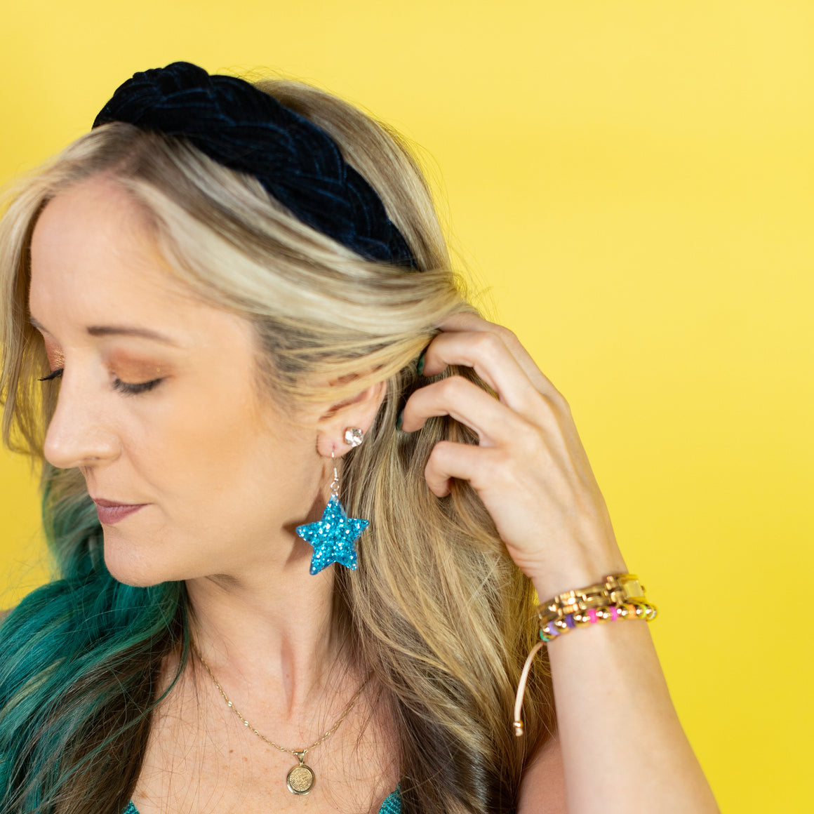 Woman wearing a teal fringe top, black headband, and colorful jewelry against a yellow background