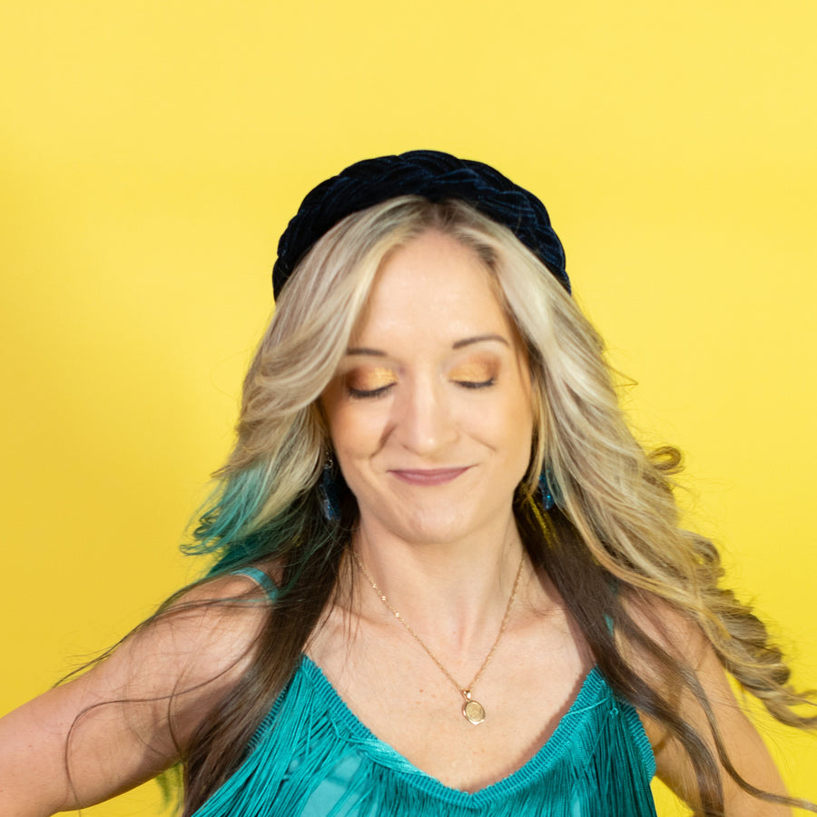 Woman wearing a teal fringe top, black headband, and colorful jewelry against a yellow background