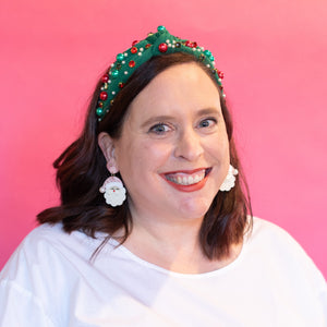Woman wearing a white top and a green headband with red decorations against a pink and purple gradient background.