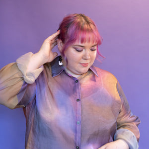 Person with pink hair wearing a sheer blouse and pink skirt against a purple background