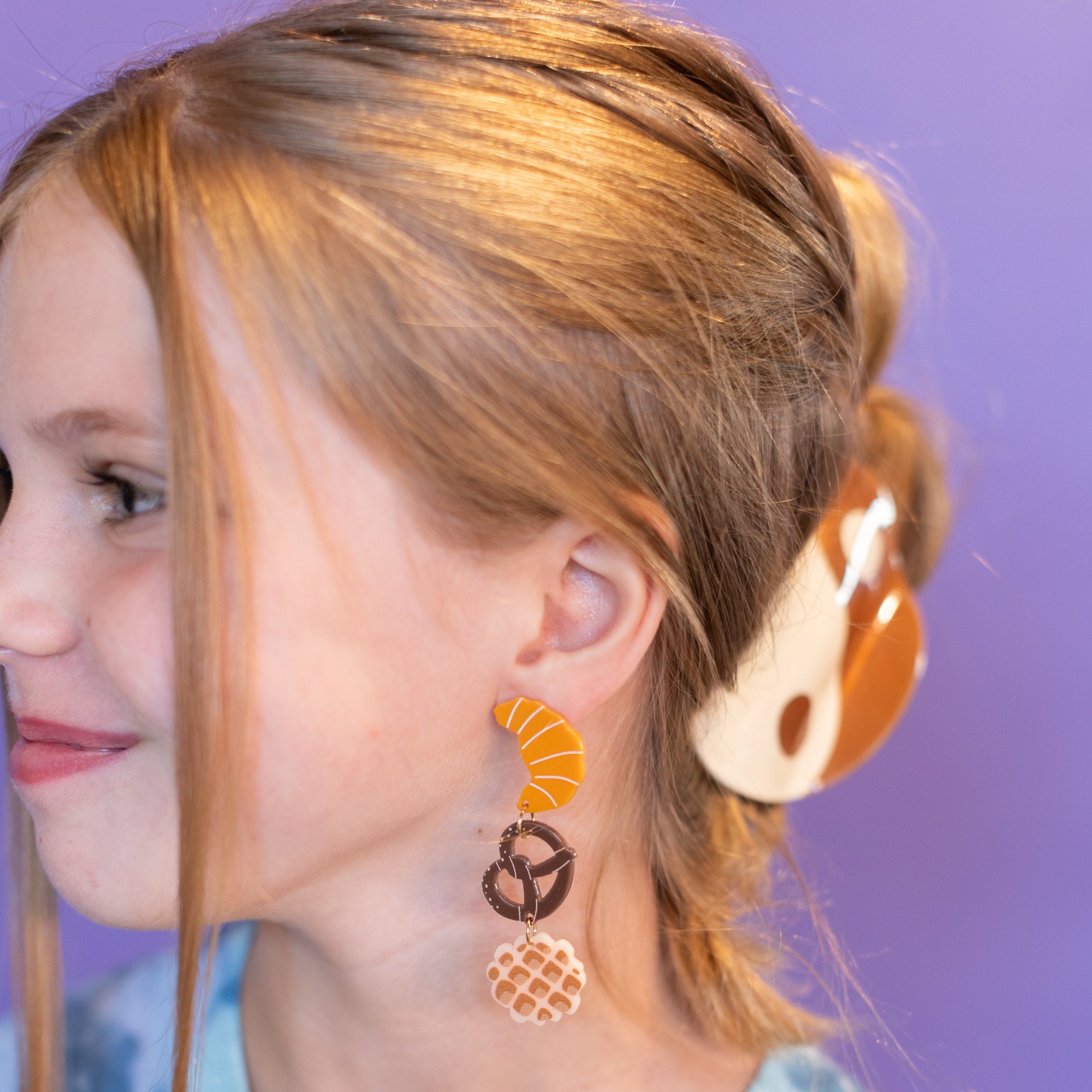 Young girl wearing colorful earrings with a purple background