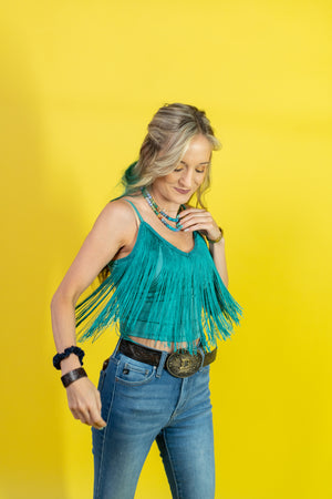 Woman wearing a teal fringe top and blue jeans against a yellow background