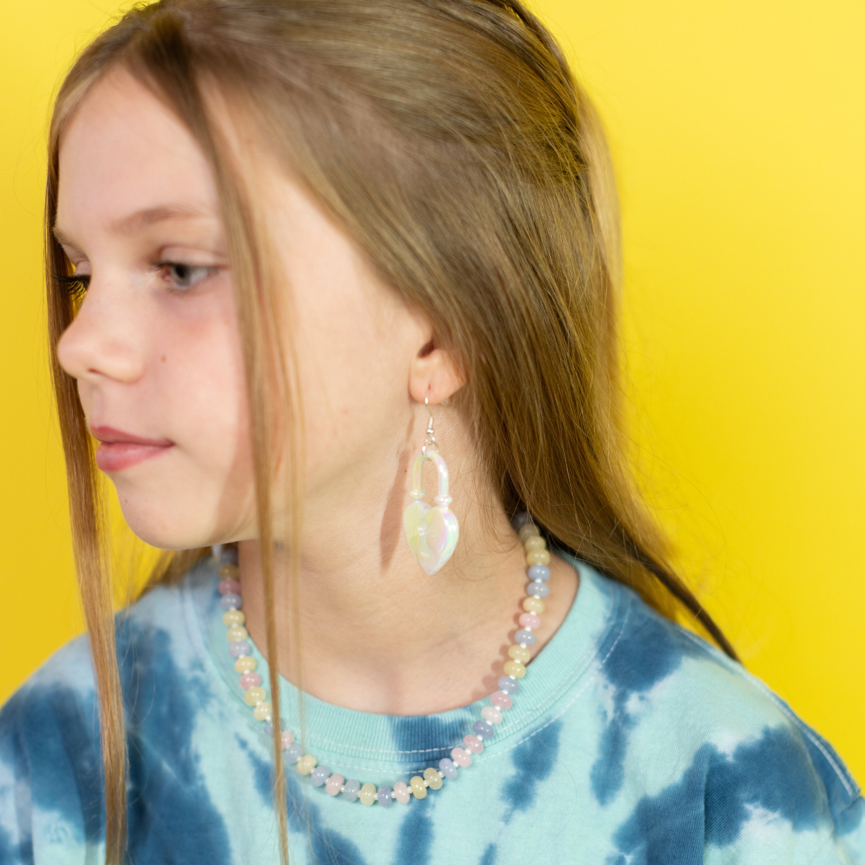 Girl wearing a blue tie-dye shirt with necklaces and earrings against a yellow background
