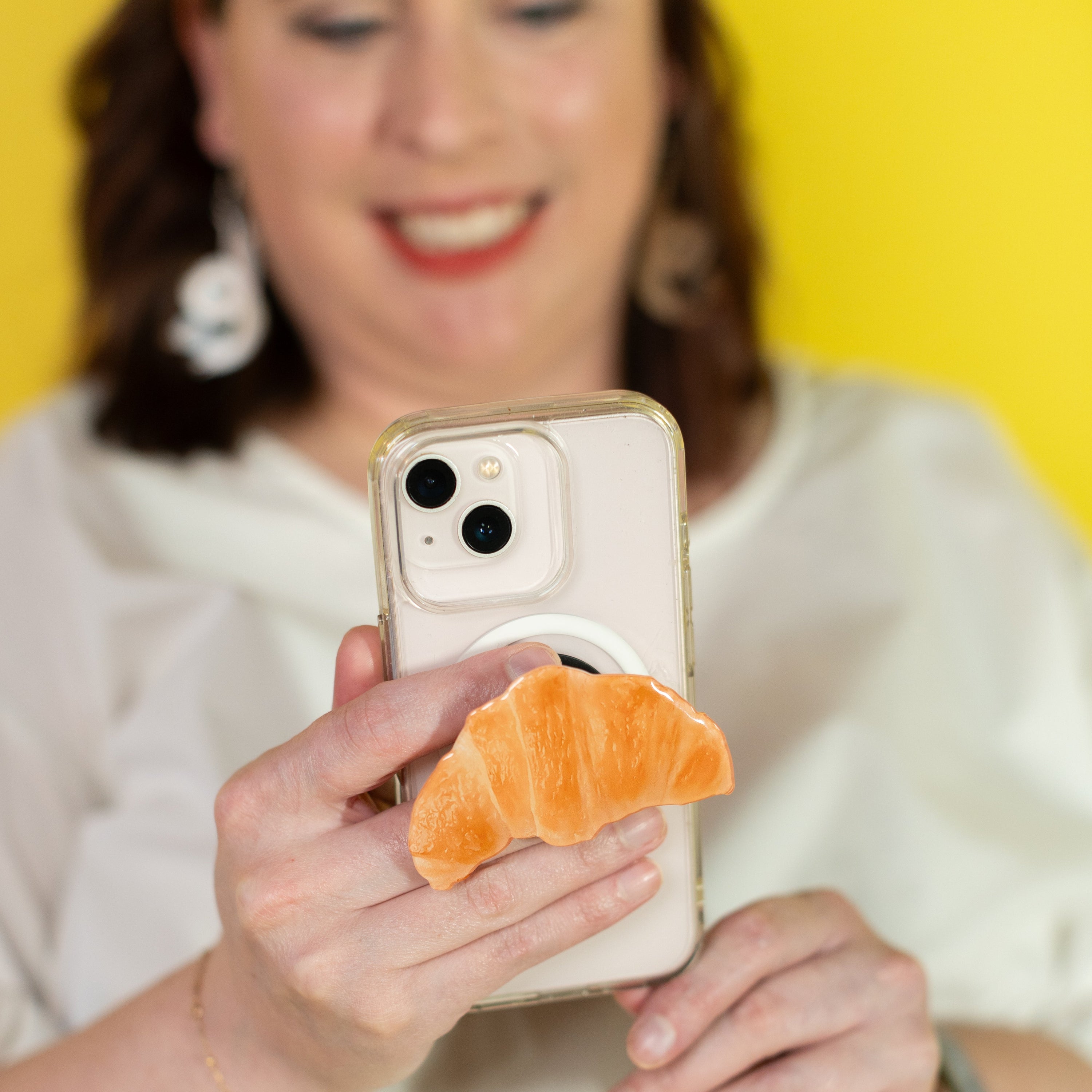Woman holding a phone with a croissant-shaped phone stand against a yellow background