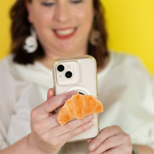 Woman holding a phone with a croissant-shaped phone stand against a yellow background